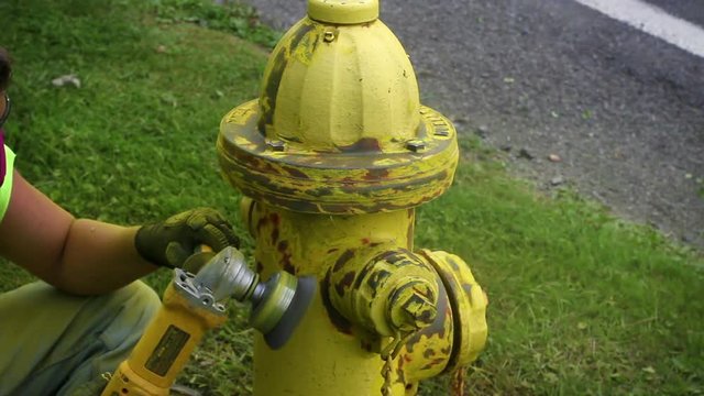 A municipal utility worker is sanding down a yellow fire hydrant V1