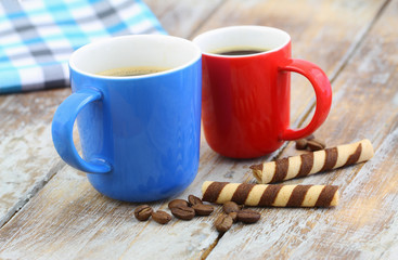 Two colorful coffee mugs and crunchy wafers on rustic wooden surface
