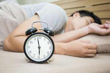 Mlarm clock on bed with man sleeping at morning.
