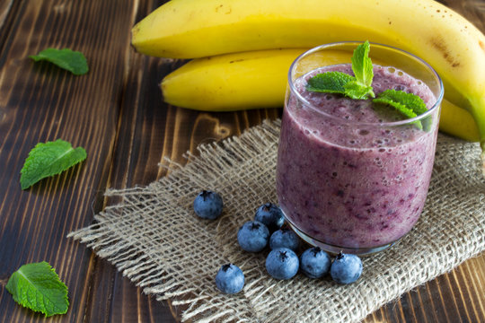 Smoothie from banana and blueberries on the brown wooden background 