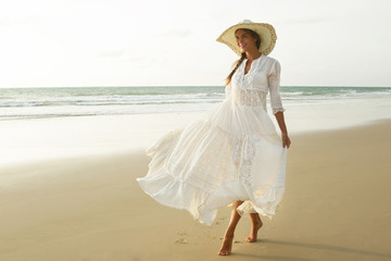 Fototapeta na wymiar Woman wearing beautiful white dress is walking on the beach during sunset