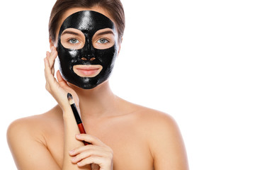 Beautiful woman is applying purifying black mask on her face