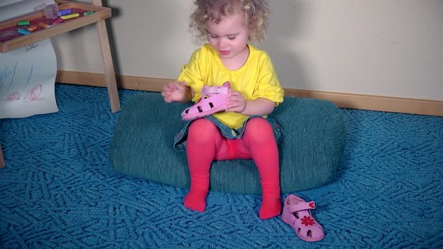 Nervous girl playing with her shoes. Child cant put sandal on