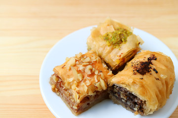 Plate of three types of Baklava sweets served on wooden table, selective focus with free space for text and design 