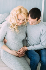 Pregnant girl with her husband sitting on bed