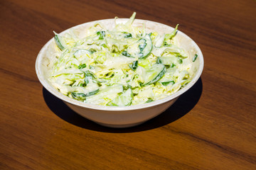 Spring salad with cabbage, cucumber, green onion, parsley and mayonnaise on wooden table