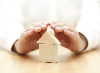 Wooden toy house protected by hands 