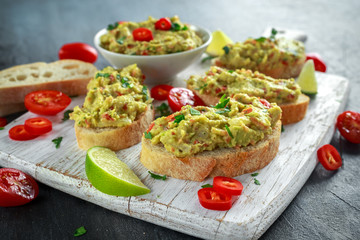 Homemade Guacamole toast with chili pepper, parsley on white wooden board