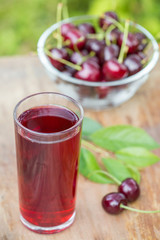 A glass of cherry juice and bowl of cherries on the table in garden outdoors