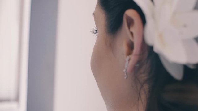 Portrait of young beautiful brunette woman with a white flower in her hair. Side view from the rear. Close up, slow motion. Woman with beautiful make-up and hairstyle. Morning of the bride