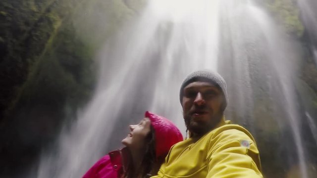 Young happy traveling couple taking a selfie on gopro camera. Man and woman near the Gljufrabui waterfall in Iceland.