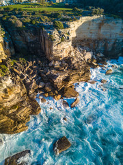 Aerial view of wave breaking in Diamond Bay rock cliff