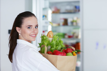 Young woman holding grocery shopping bag with vegetables .Standing in the kitchen. Woman in the kitchen looking at the camera