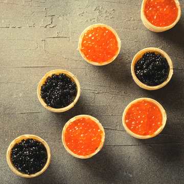 Black and red caviar tartlets, appetizer canapes on gray background, top view, toned