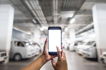 The hands are holding the blank white screen smart phone in the parking lot of the department store. Hands holding smart phone To locate a parked car in the parking lot of a department store.