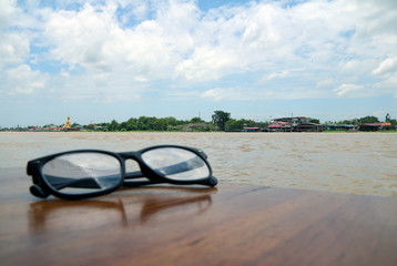 Beautiful view of Chaophraya River and foreground out focus, Glasses placed on the wooden table, many white cloud on the blue sky.