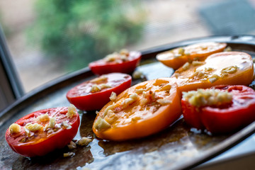 Yellow and red tomato slices on a baking tray, ready to go in the oven. Topped with garlic, salt and olive oil.

