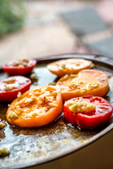 Yellow and red tomato slices on a baking tray, ready to go in the oven. Topped with garlic, salt and olive oil.

