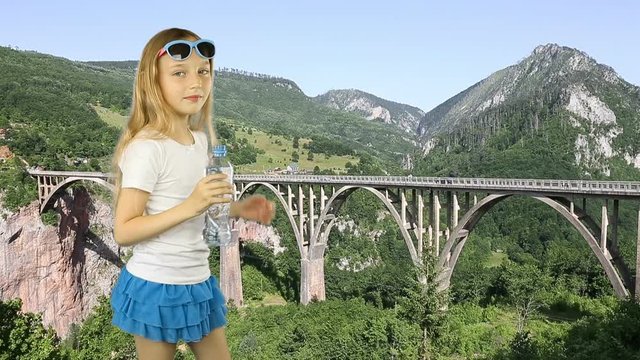 Young girl standing on green grass valley and drinking clear fresh water summer day. Trees mountines valley and Tara bridge on background. Have same clip with transparent background Alpha Channel.