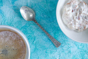 Breakfast. Coffee and fruit yogurt in a white bowl on a turquoise background.Top view.