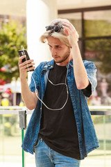 Hipster man standing on city street listening music