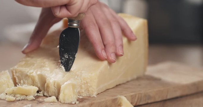 Slow motion slide of female hand cutting hard parmesan cheese
