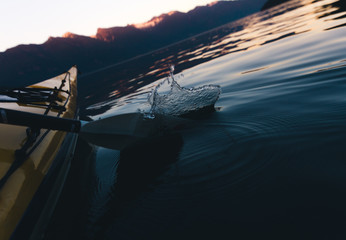 Water splash with paddle while kayaking alone on calm water with mountains in the background while sunset