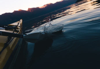 Water splash with paddle while kayaking alone on calm water with mountains in the background while...