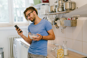 Man eating healthy breakfast and texting message  in his kitchen