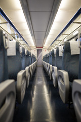 Obraz premium Empty interior of a passenger train car aka coach or carriage . Rows of unoccupied seats and folding tables in economy or second class.