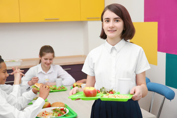 Cute girl holding tray with delicious food in school canteen