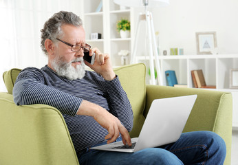 Handsome elderly man sitting in armchair with laptop