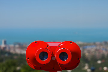 Bright red coin operated binoculars on the panoramic view of the city Batumi from rooftop platform...