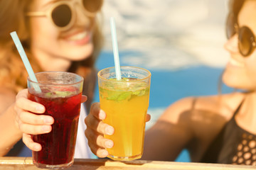 Beautiful young women clinking glasses with cocktails while relaxing in pool, closeup