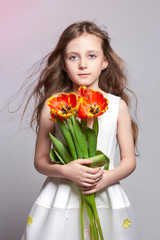 Fashion red-haired girl with tulips in hands. Studio photo on light coloured background. Birthday, holiday, mother's day, first day of school