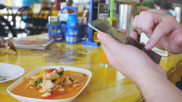 Client photographs liked the dish on a mobile phone. Take a photo of tom yam thai soup in a restaurant with mobile phone camera for social network while traveling in Thailand