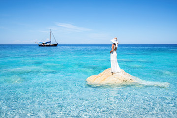 Elegante Frau in weißen Abendkleid steht träumend auf einen Felsen im Mittelmeer