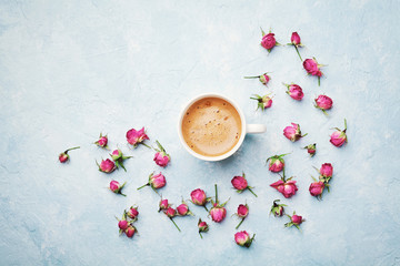 Morning coffee cup and dry rose flowers on blue vintage table top view in flat lay style. Cozy breakfast on Mother or Woman day.