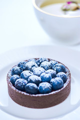 Hand made dessert tarlets from pistachio and chocolaty bakery dough with blueberry decoration served on plate with cap of tea