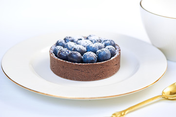 Hand made dessert tarlets from pistachio and chocolaty bakery dough with blueberry decoration served on plate with cap of tea
