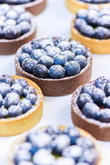 Hand made tarlets dessert from pistachio and chocolaty bakery dough with blueberry decoration on white background