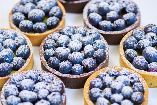 Hand made tarlets dessert from pistachio and chocolaty bakery dough with blueberry decoration on white background
