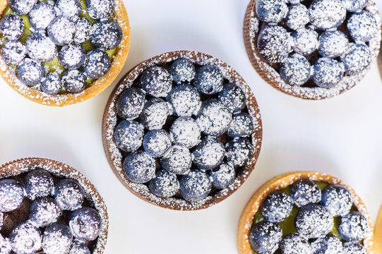 Hand made tarlets dessert from pistachio and chocolaty bakery dough with blueberry decoration on white background