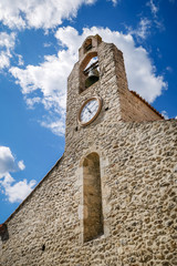 Fototapeta na wymiar Picturesque medieval stone church in south of France at traditional catalan village of Laroque des Albères, beautiful bell tower with cloudy sky background