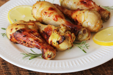Grilled chicken legs with mustard on wooden table served on white plate with rosemary. BBQ dinner background