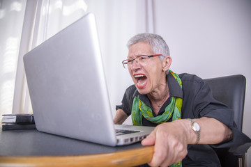Senior old woman screaming at her laptop, enraged with news
