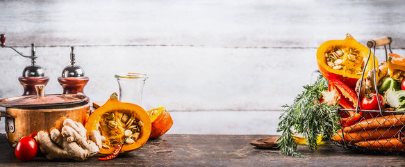 Autumn seasonal  cooking concept. Various autumn seasonal organic vegetables: pumpkin,carrot,paprika,tomatoes,ginger in basket on wooden kitchen desk tables with pot at wall background, front view.