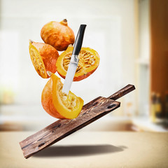 Flying pumpkin  with wooden cutting board and knife at desk table at kitchen background. Sliced pumpkin , cooking preparation. Healthy organic seasonal food or diet eating  concept.
