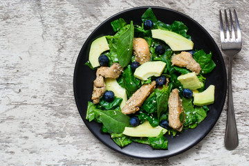 Chicken salad with avocado, spinach and blueberries in black plate with fork