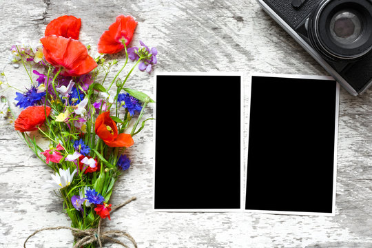 Retro camera and blank paper photo frames on wooden table with summer wildflowers